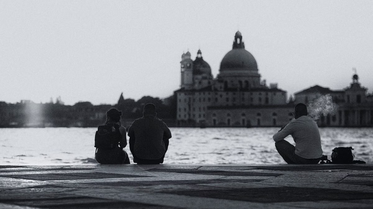 Silhouette of people sitting by the water in Venice, Italy, with historic architecture in the background.